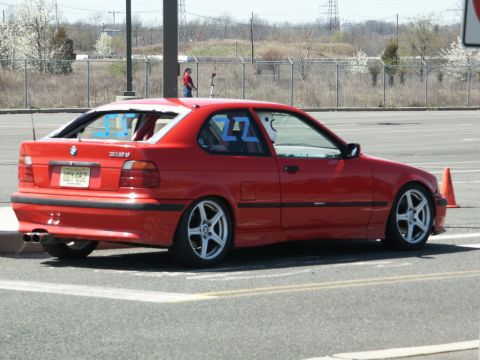 2001 Mercury Grand Marquis - A red BMW 318ti is parked on a paved surface, possibly at a track event, with a roll cage visible inside.