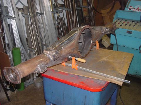 1979 Ford Bronco - A rusty rear axle housing is secured with clamps on a workbench, with a control panel machine nearby.