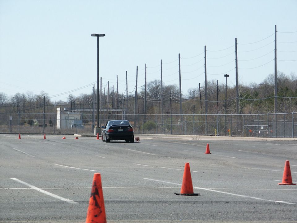 Black sedan seen from the rear on a paved lot with orange cones