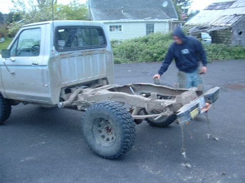 1983 Ford Ranger - A person works on the chassis of a Ford truck that is missing its bed and engine.