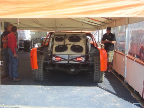 1990 Ford Bronco - rear of an off-road race truck with orange fenders shows four large cooling fans mounted in the bed under a pit canopy.