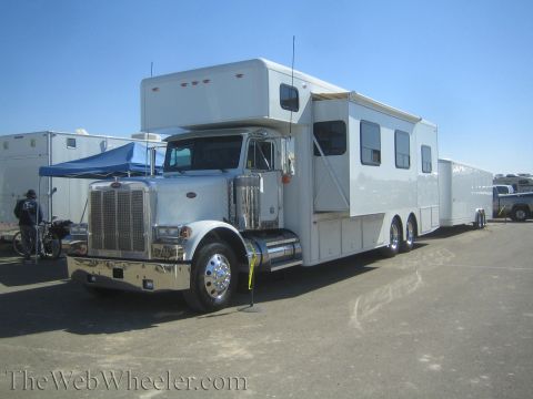 1990 Ford Bronco - white Peterbilt semi tractor coupled to a long toterhome trailer is parked in a dirt paddock with a pop-up tent alongside.