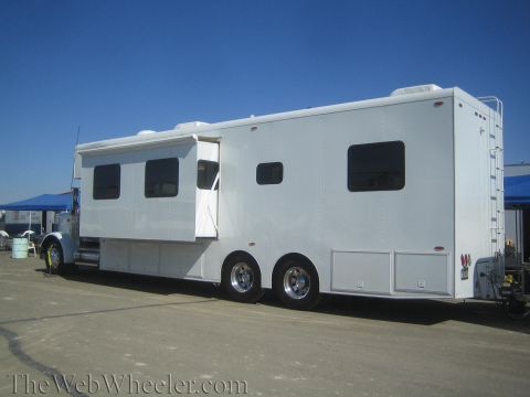1990 Ford Bronco - side of a long white toterhome trailer with windows and an open awning door sits in a dirt paddock.
