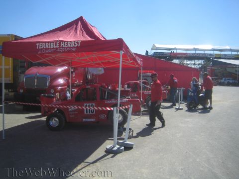 1990 Ford Bronco - Terrible Herbst Motor Sports pit area with a red number 119 off-road race truck parked beneath red tents as crew members in red shirts stan…