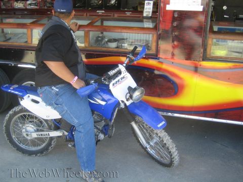 1990 Ford Bronco - person sits on a blue and white Yamaha dirt bike parked beside a trailer with orange flame graphics.