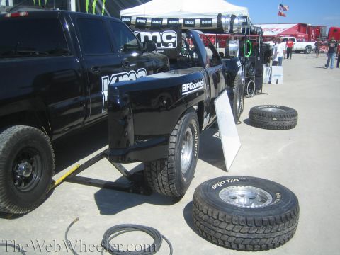 1990 Ford Bronco - black pickup truck sits on a display stand with off-road tires laid out around it at an outdoor KMC and BFGoodrich vendor booth.