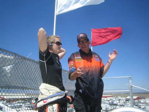 1990 Ford Bronco - young woman in a black racing suit and a man in an orange crew jacket talk on an observation platform beside white and red flags.