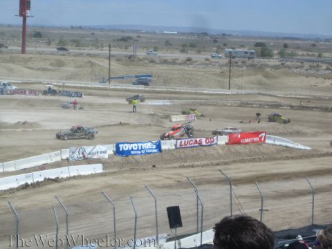 1990 Ford Bronco - Off-road race trucks run a banked dirt track lined with Toyo Tires and Lucas Oil banners, viewed over spectators from the grandstands.