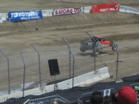 1990 Ford Bronco - red and silver tube-frame off-road race truck drives a dirt course backed by Toyo Tires and Lucas Oil banners.