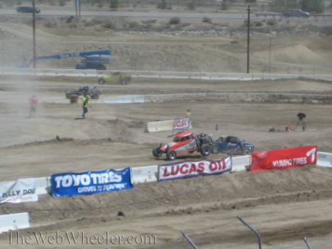 1990 Ford Bronco - Off-road race trucks battle through a dusty dirt turn lined with Toyo Tires and Lucas Oil sponsor banners.