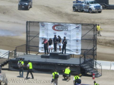 1990 Ford Bronco - Racers stand on a Championship Off-Road Racing victory podium as crew in safety vests gather below.