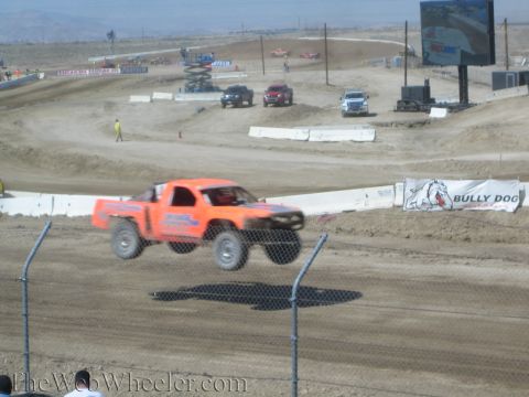 1990 Ford Bronco - orange off-road race truck flies through the air over a dirt course beside a Bully Dog sponsor banner.