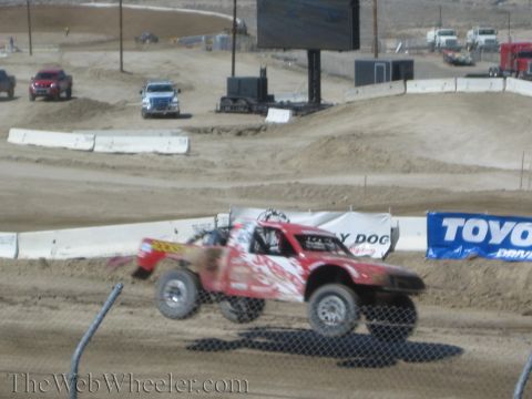 1990 Ford Bronco - red number-300 off-road race truck slides through a dirt corner past a Toyo Tires banner.