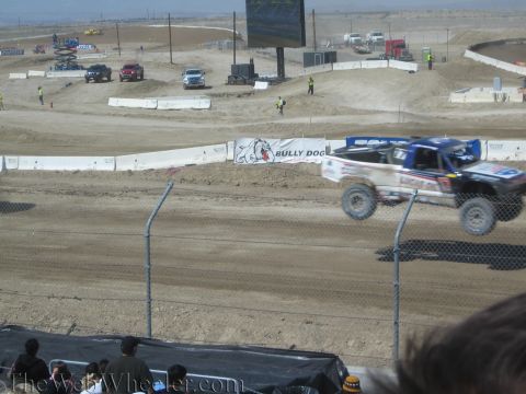 1990 Ford Bronco - white and blue off-road race truck catches air on a desert dirt course beside a Bully Dog banner.