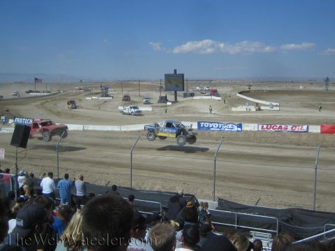 1990 Ford Bronco - Two off-road race trucks race along a dirt short-course track lined with Toyo Tires and Lucas Oil banners.