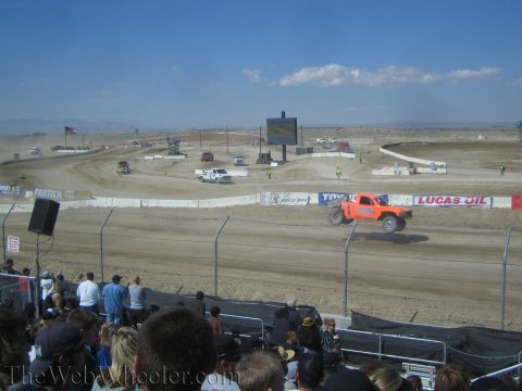 1990 Ford Bronco - orange off-road race truck rounds a dirt short-course track past Lucas Oil and Toyo Tires banners.