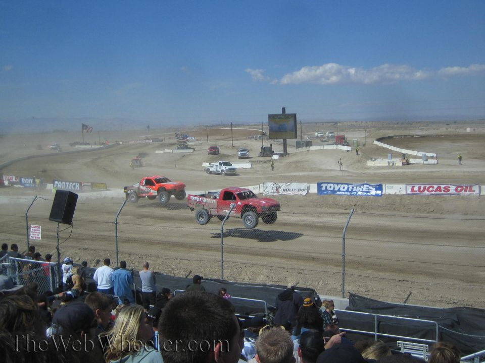 Two orange and red off-road race trucks on a dirt short-course track