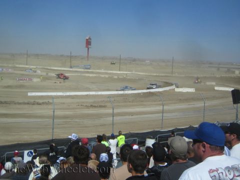 1990 Ford Bronco - distant view of a dusty dirt short-course track with race vehicles and a crowd of spectators in front.