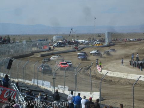 1990 Ford Bronco - Multiple off-road race trucks are spread across a dusty dirt short-course track during a desert race.