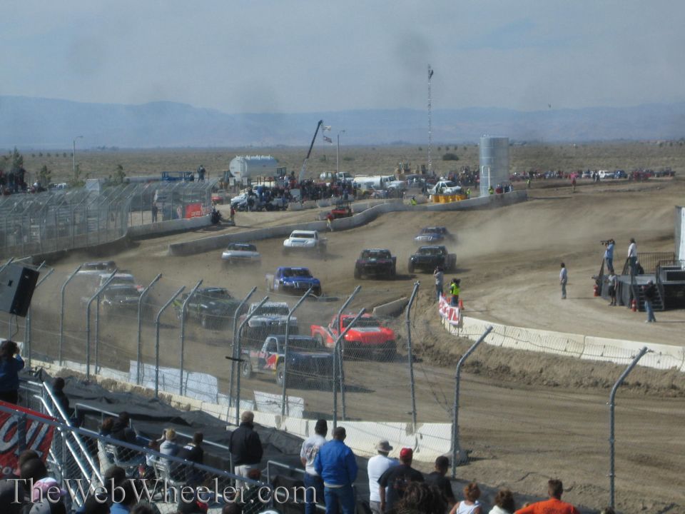 Field of off-road race trucks racing on a dusty dirt short-course track