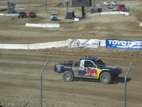 1990 Ford Bronco - dark blue Red Bull-liveried off-road race truck races down a dirt straight past Toyo Tires and Bully Dog banners.