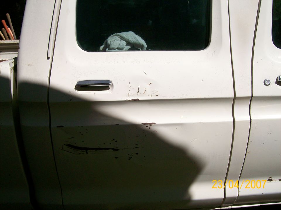 Side view of a white pickup truck's doors. Some damage and scratches are visible on the lower door panel