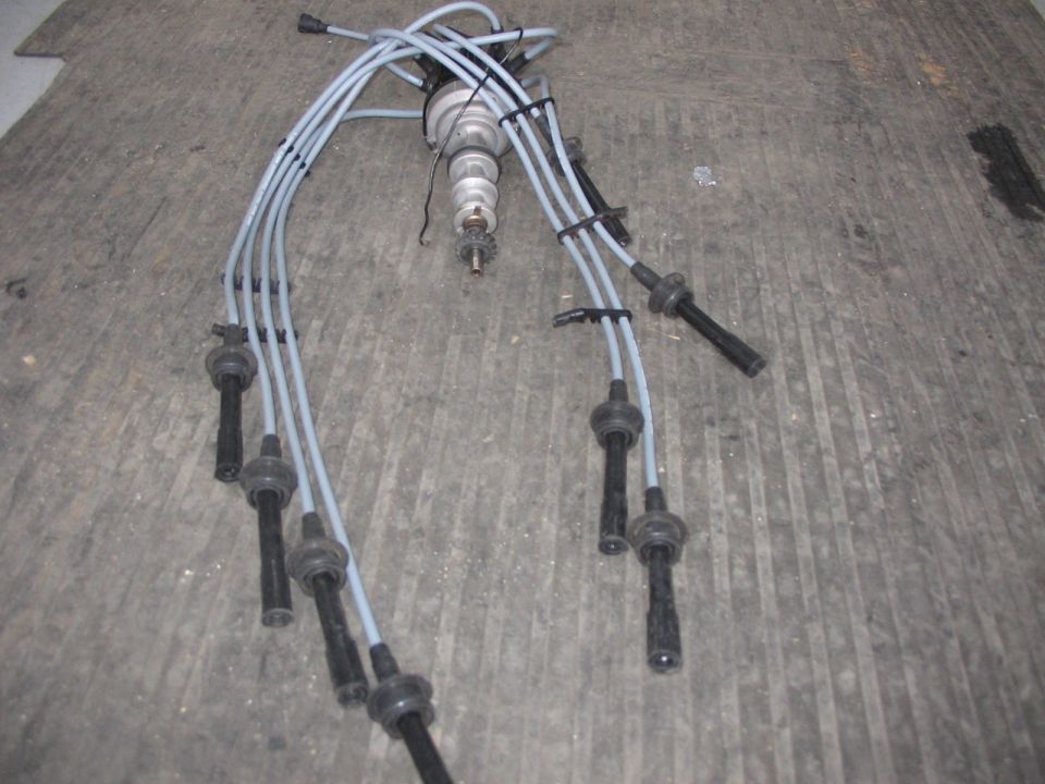 Distributor with spark plug wires on a concrete floor. Supermotors.net logo in corner