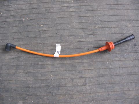 1964 Ford 427 - A single orange spark plug wire with black and red boots is displayed on a wooden surface.
