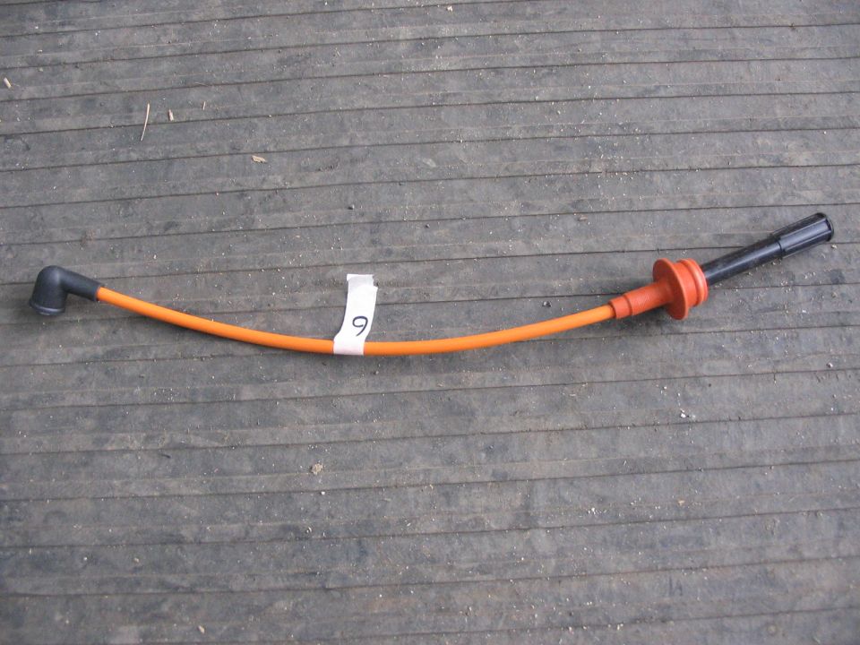 Orange spark plug wire with black and red boots on wooden planks