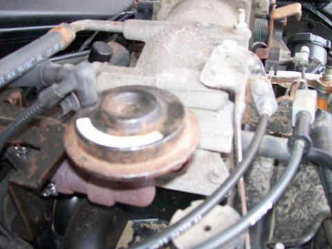 1999 Ford Crown Victoria - Close-up of an engine vacuum actuator, likely from a Ford Crown Victoria, with a white label visible.