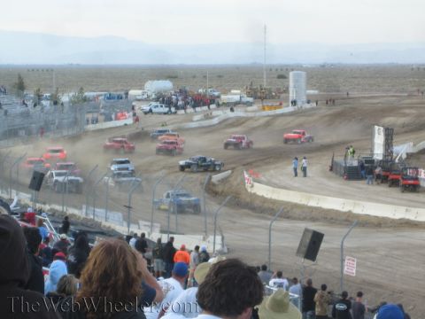 1990 Ford Bronco - pack of off-road race trucks kicks up dust on a desert dirt short-course track.