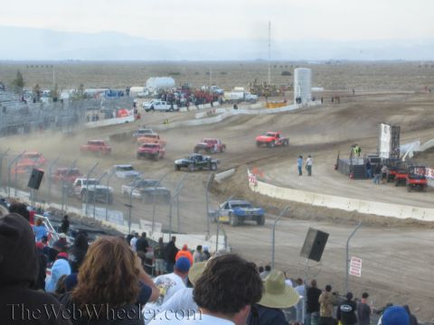 1990 Ford Bronco - Off-road race trucks raise dust on a dirt oval as spectators watch from the stands.