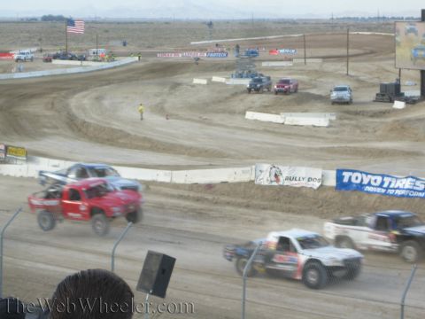 1990 Ford Bronco - Off-road race trucks corner on a banked dirt track lined with Toyo Tires and Bully Dog banners.