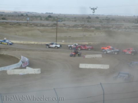 1990 Ford Bronco - line of off-road race trucks runs the dirt course while a camera drone flies above.