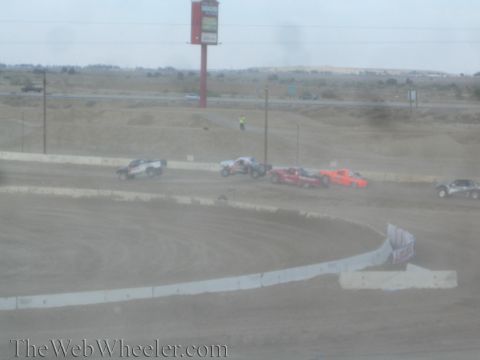 1990 Ford Bronco - Off-road race trucks round a dusty dirt course beneath a tall red billboard.