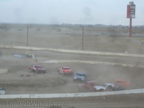 1990 Ford Bronco - Off-road race trucks bunch together raising dust on a desert dirt short-course track.
