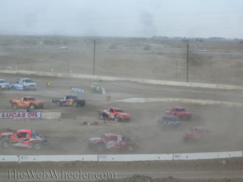 1990 Ford Bronco - Off-road race trucks crowd a dirt course in dust beside a Lucas Oil banner.