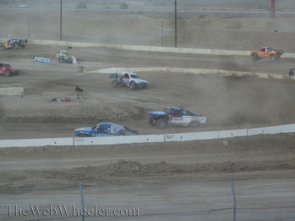 Off-road race trucks racing through dust on banked dirt track