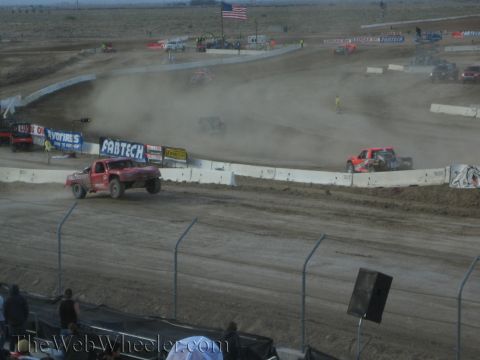 1990 Ford Bronco - red off-road race truck rounds a dusty dirt course lined with Fabtech and Toyo Tires banners.