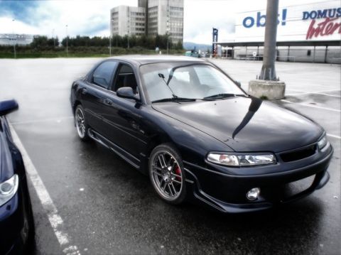 1995 Ford Probe - A black sedan with aftermarket wheels and red brake calipers is parked in a wet lot.