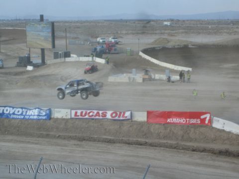1990 Ford Bronco - off-road race truck catches air over a jump on a wide desert short-course track past Toyo Tires and Lucas Oil banners.