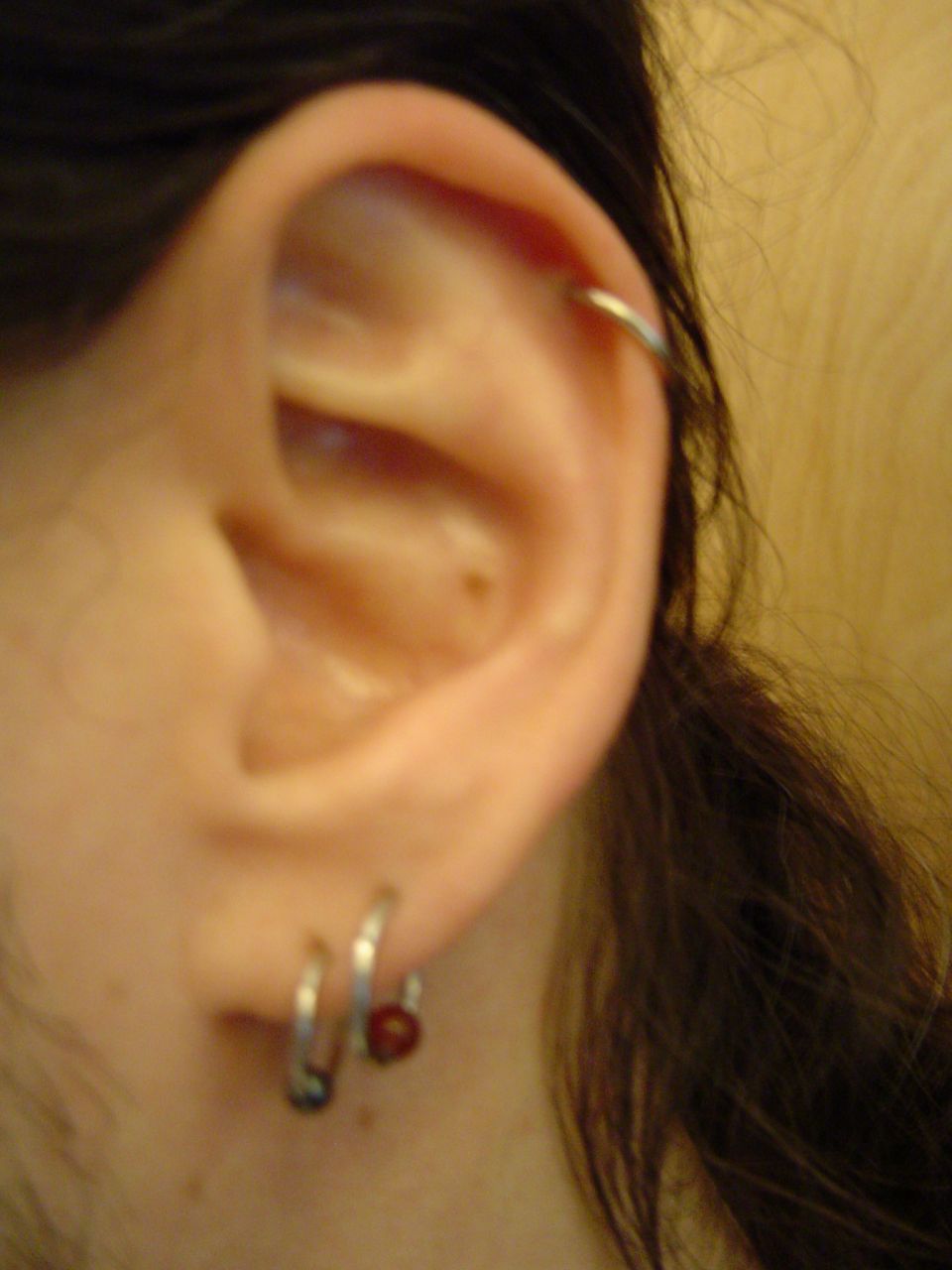 Close-up of a human ear with multiple piercings, including a hoop in the upper cartilage and two hoops in the lobe