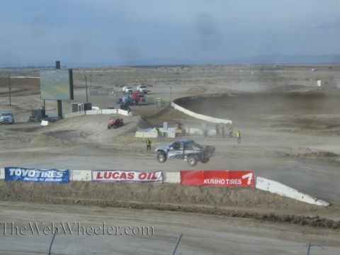 1990 Ford Bronco - blue off-road race truck runs a wide desert short-course track past Toyo Tires, Lucas Oil and Kumho Tires banners.