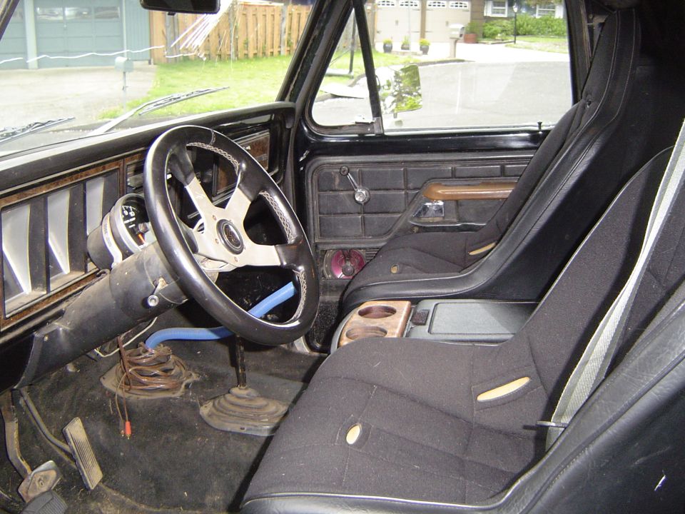 Interior view of black vehicle with bucket seats, custom steering wheel, and floor shifter