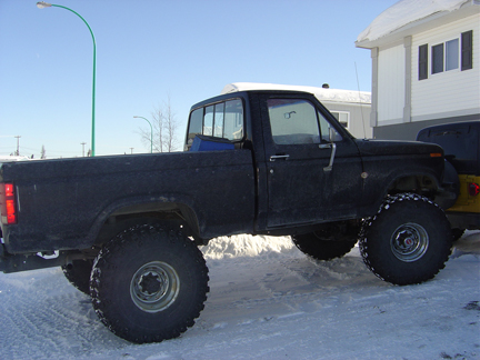 1986 Ford F-150 - A modified black pickup truck with oversized tires sits in a snowy environment next to another vehicle.