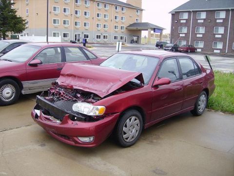 1996 Ford F-350 - A red sedan with significant front-end damage is parked on a wet surface, with another vehicle visible behind it.