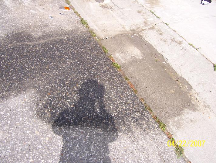 Shadow of a person holding a camera on a wet asphalt and concrete surface. Date stamp '04/22/2007' is visible