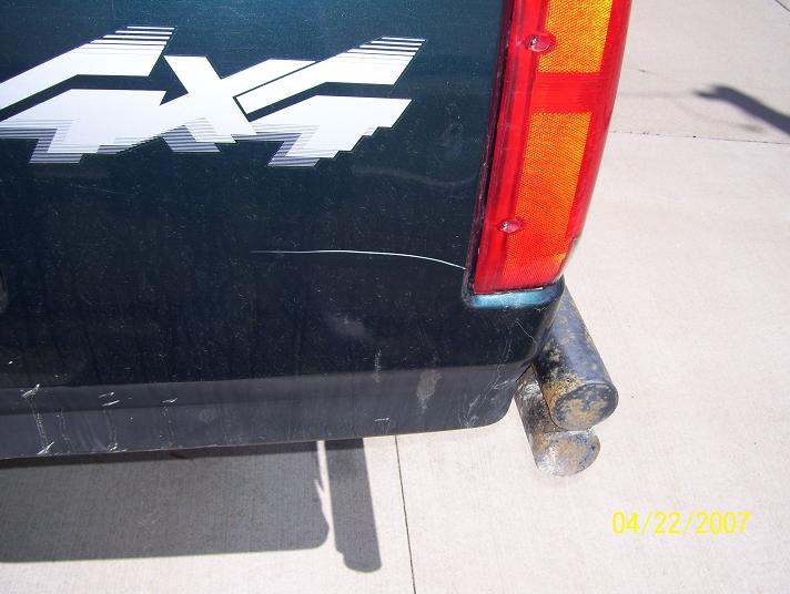 Dark green truck rear quarter panel with a white 4x4 decal and a red taillight. Dual exhaust pipes are visible below