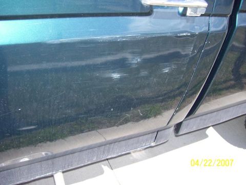 1996 Ford F-350 - The side of a dark green 1996 Ford F-350 pickup truck shows significant damage, including numerous scratches on the door panel.