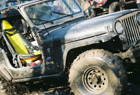 1981 Jeep CJ7 - A muddy Jeep CJ navigates off-road terrain, with another vehicle visible in the background.